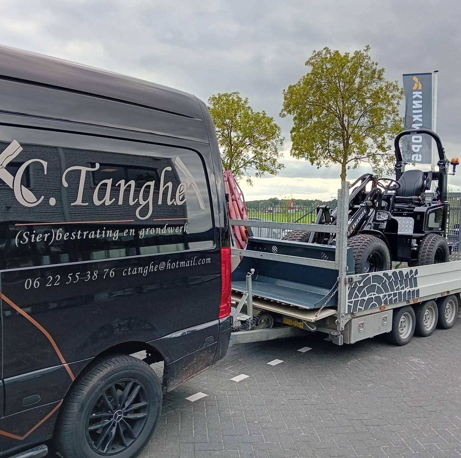 Zwarte bus met de belettering C.Tanghe (Sier)bestrating en grondwerk, met een machine op de aanhanger