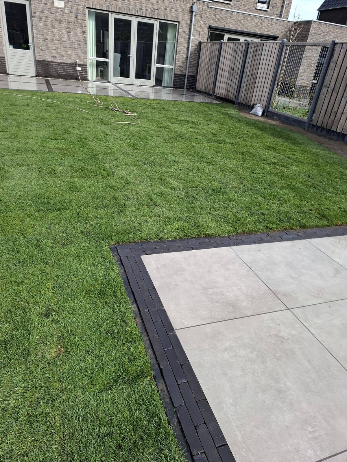 Terras van grote tegels met een donkere rand naast vers gras