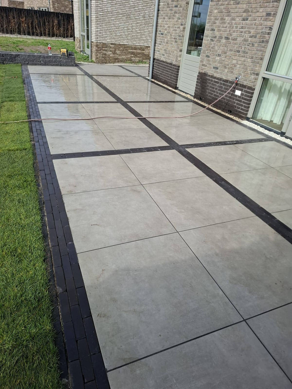 Tegelpad met donkere rand tussen gras en de gevel van de woning