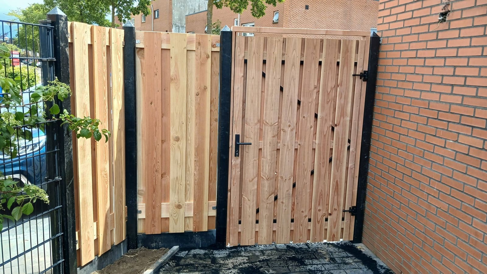 Nieuwe houten schutting met een houten poort naast een bakstenen muur