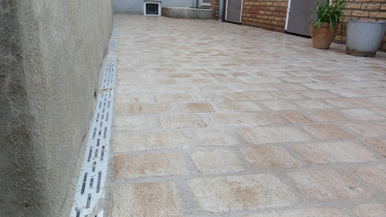 Binnenplaats in lichte sierbestrating met afvoergoot langs de muur en potten met planten