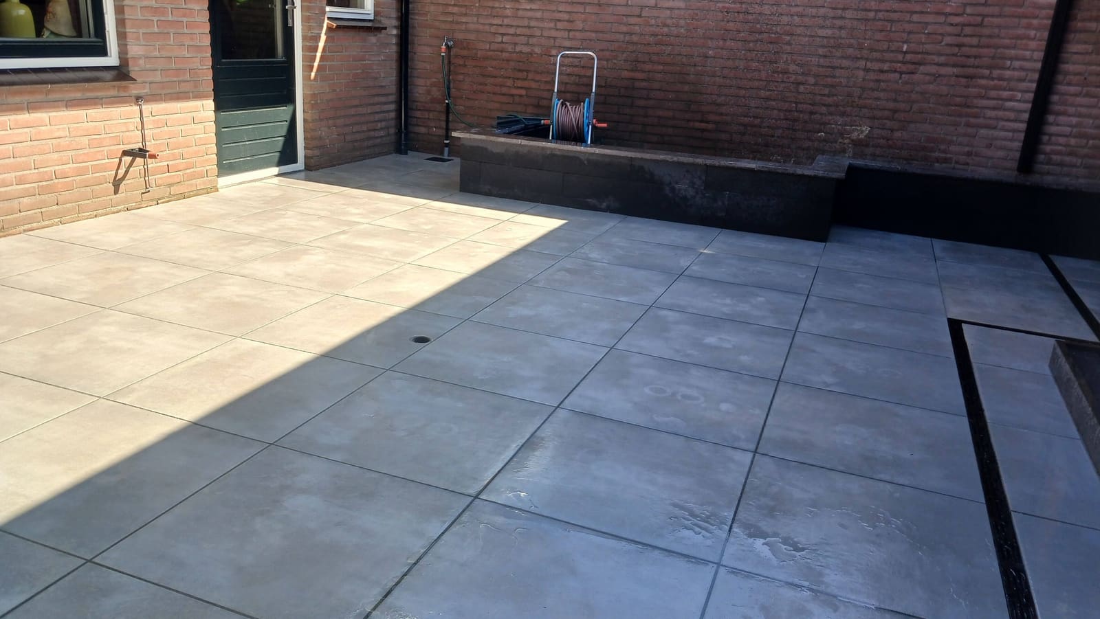 Terras van grote tegels tegen het huis met een plantenbak