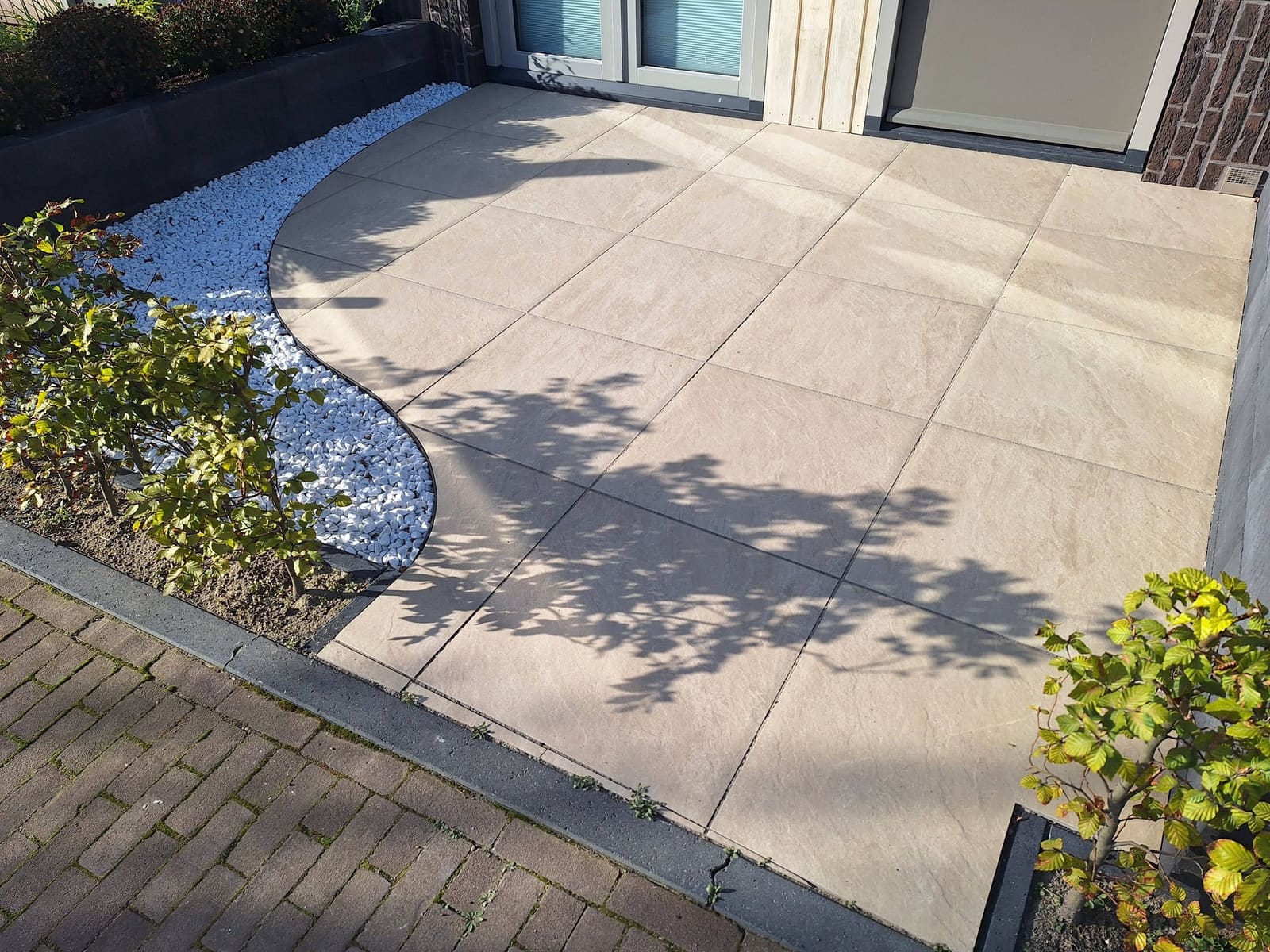 Voortuin met grote lichte tegels in een ronde vorm, omzoomd door wit grind en planten